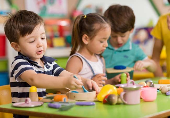 three preschoolers participating in a group activity at a green table