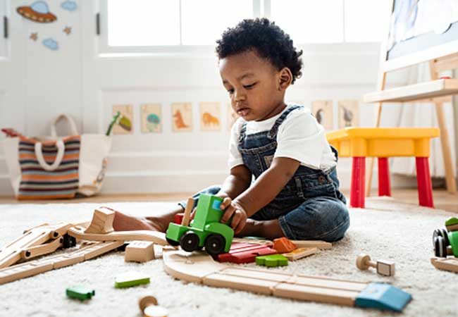 an infant participating in sensory activities by playing with a wooden toy truck on a soft carpet
