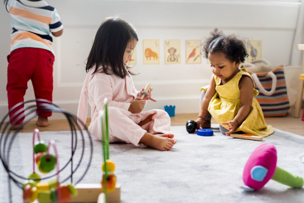 two children sitting on a carpet and playing with toys at a child care center