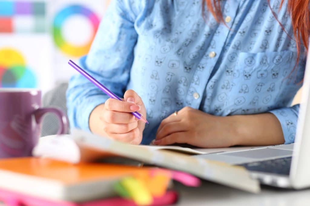 a woman jots down notes using a purple colored pencil