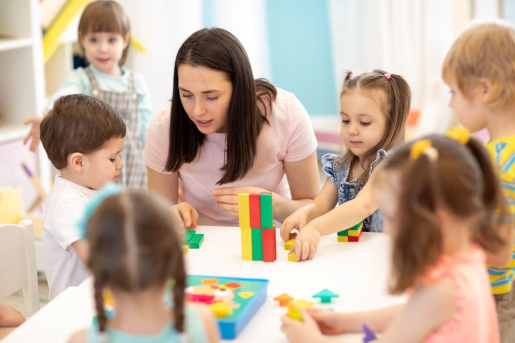 a preschool teacher surrounded by toddlers playing with blocks