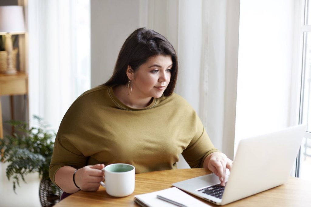 a woman works on her computer, cup of coffee cup in hand