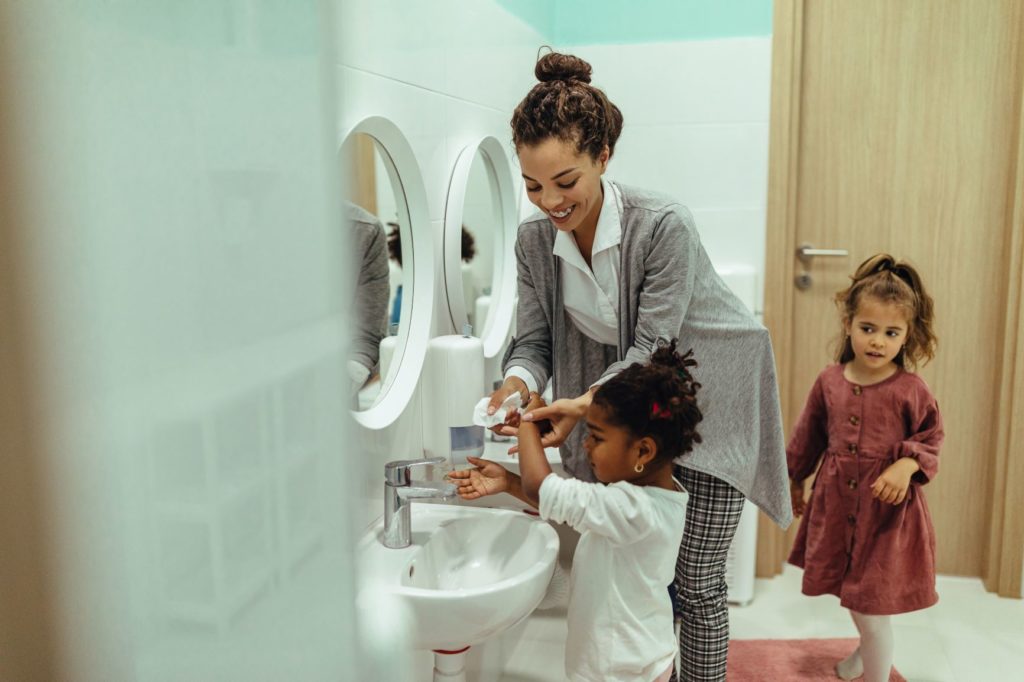 a woman helps two girls wash their hands