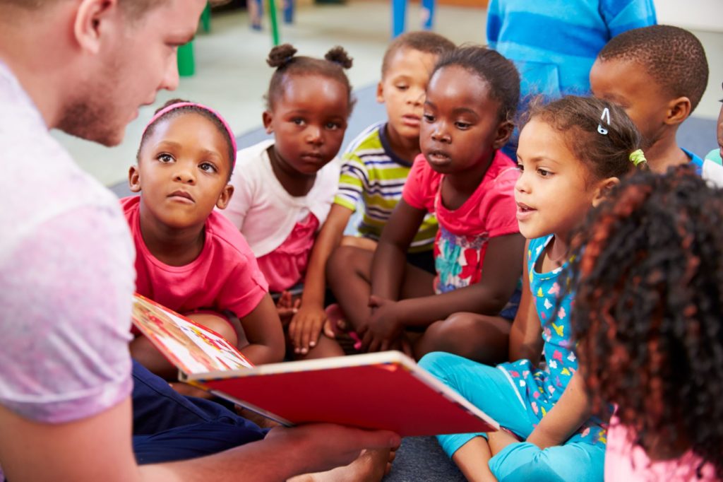 a teacher reads a book to children gathered around them at a daycare center