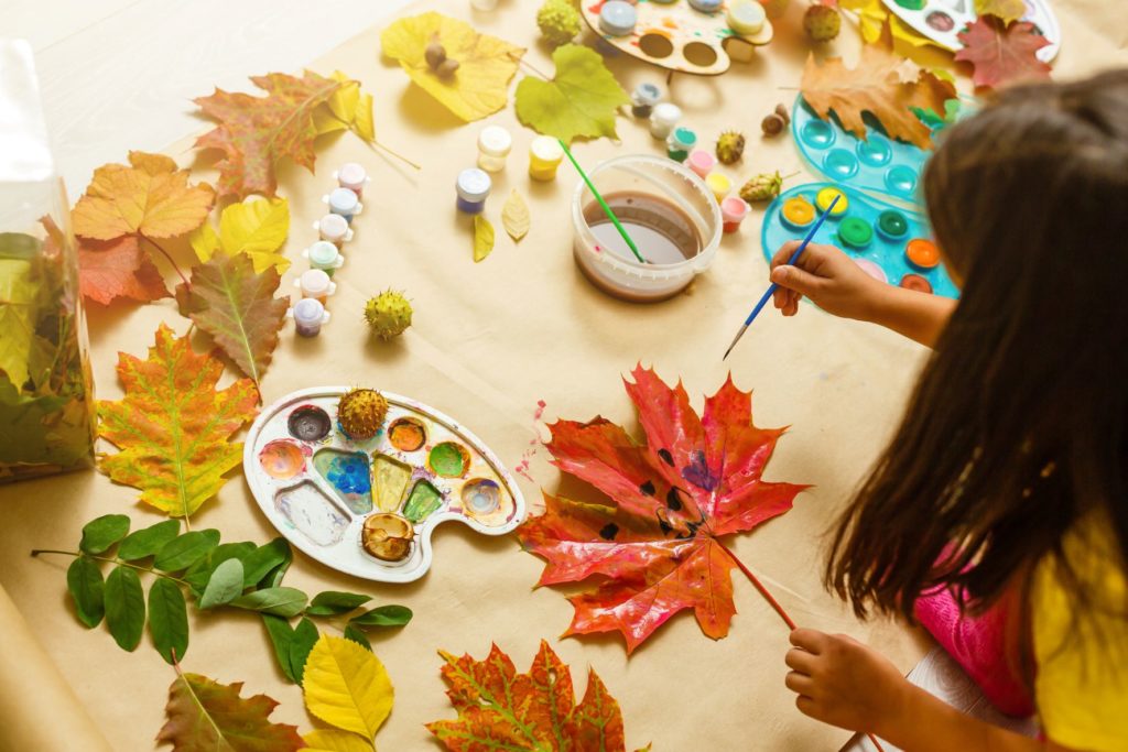 a preschooler participating in an invigorating fall activity: painting faces onto autumn leaves