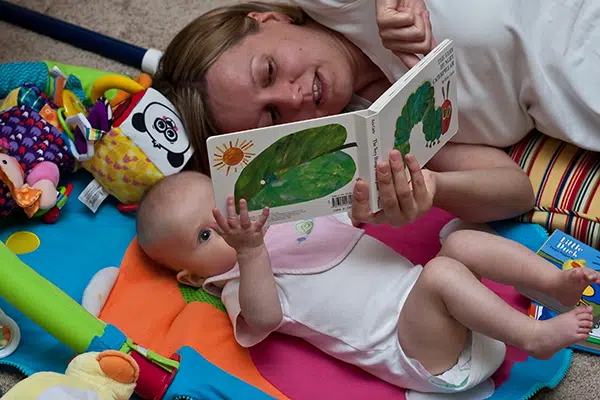 Teacher reads book to baby while laying on the floor.