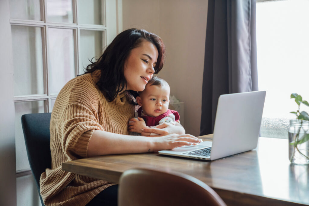 Mom uses a computer while holding her baby.