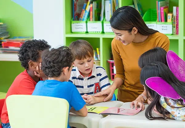 Preschool teacher explains sight words to children - a book is open with the letters A and B on the table. 