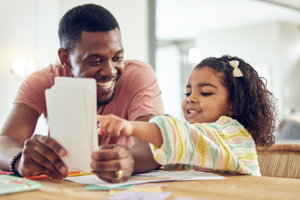 Man uses flashcards to teach literacy skills to young girl.