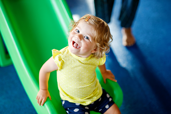 preschooler smiles up at camera while sliding down a green slide