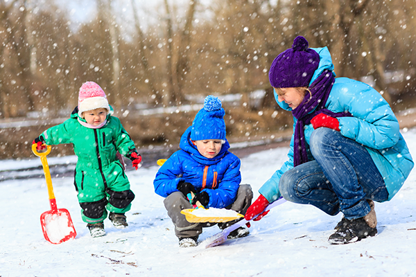 Preschool teacher plays with children in the snow.