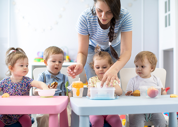 Woman feeds lunch to toddlers in a daycare.